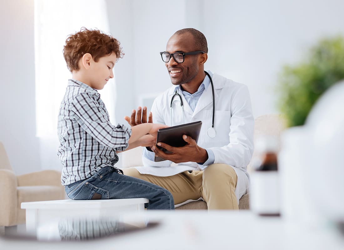Employee Benefits - Friendly Doctor Giving a Young Boy a Check-up in His Office
