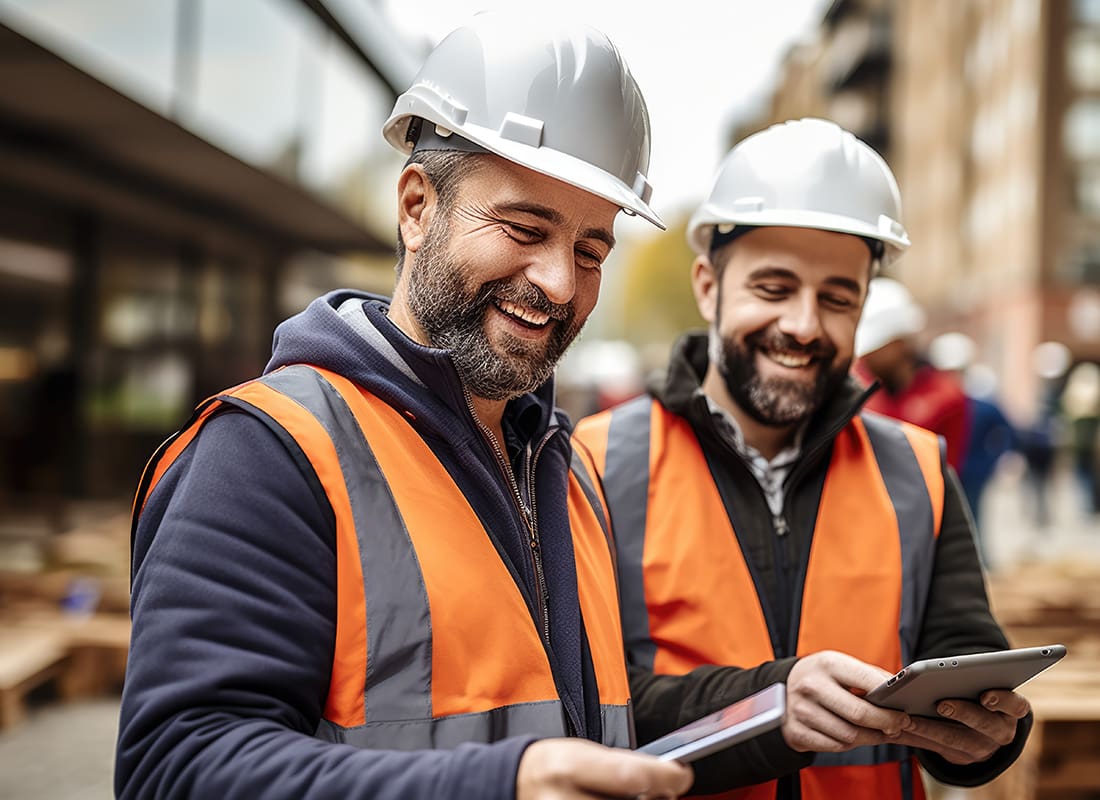 Insurance by Industry - Two Cheerful Construction Workers Reviewing Plans on Tablets at a Site